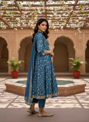Woman in a blue traditional outfit standing in an ornate courtyard with floral decorations.
