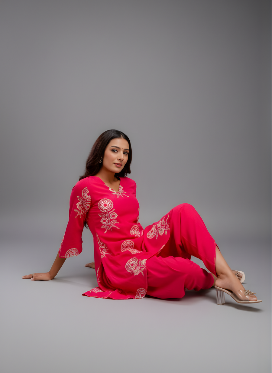 Woman in a bright pink outfit with white patterns sitting on a gray background