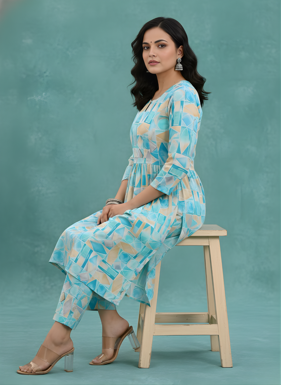 Woman sitting on a stool wearing a light blue patterned outfit against a teal background