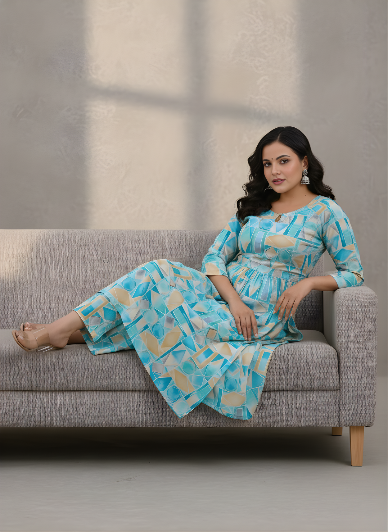 Woman in a blue and white patterned outfit sitting on a gray sofa.
