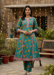 Woman wearing a colorful floral dress standing outdoors with decorative lights and plants.