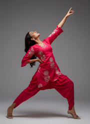 Dancer in a bright pink traditional outfit with white patterns on a gray background