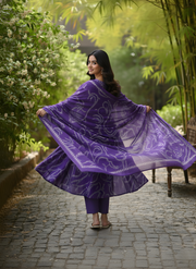 Woman in a purple traditional outfit standing in a garden with greenery.