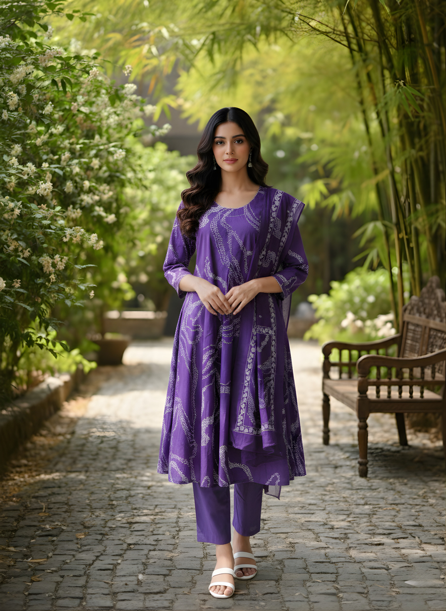 Woman in a purple outfit standing in a garden with greenery and a wooden bench.